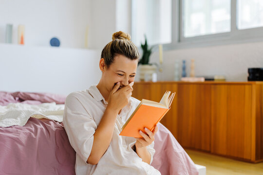 Woman laughing enjoying a funny book indoors