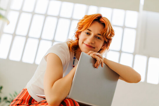 Smiling woman posing with laptop in bright creative space