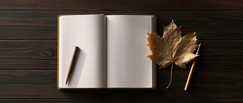 Notebook and pencils next to a maple leaf on wood background