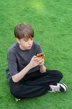 Teenager use smartphone with orange case on green grass