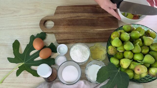 flat lay of baking ingredients on wooden table, fresh green figs in bowl, flour and sugar in glass jars, brown eggs and fig leaves, preparing homemade dessert