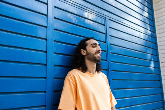 Smiling man leaning against blue urban wall in city