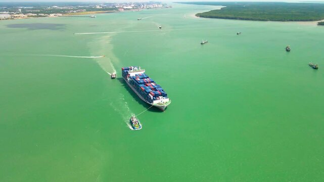 Aerial view of a container ship with tugboats sailing through the Strait of Malacca near Klang, Selangor, Malaysia.