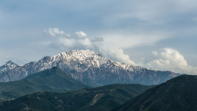Close view of a snow-capped summit towering above rolling green hills in the Chimgan Mountains of Tashkent Region, Uzbekistan.