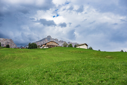 Alpine meadow and farmhouse beneath dolomites near La Villa