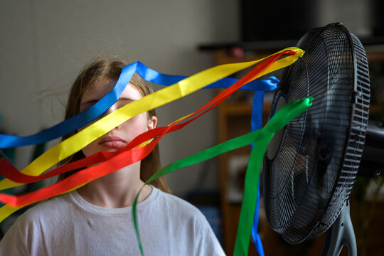 Child behind colorful ribbons blown by domestic fan