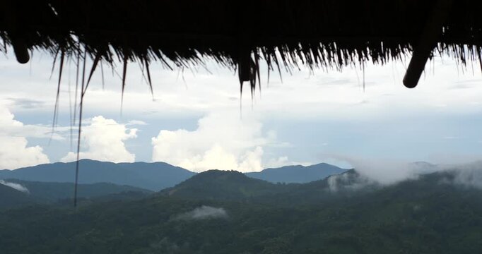 Scenic view of misty green mountains framed by rustic thatched roof eaves