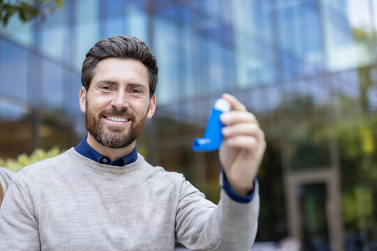 Portrait of a young man sitting on a bench on the street, holding an asthma inhaler in his hands, pointing at the camera