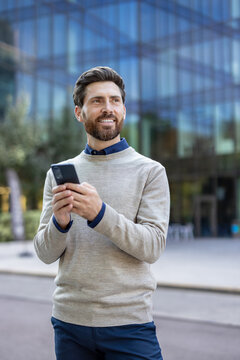 Vertical photo of a young man standing on the street in an office block and using his mobile phone