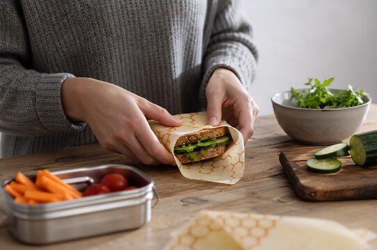 Woman preparing a healthy lunch with sandwich, salad, vegetables, and meal container on a wooden table. Balanced nutrition and calorie conscious food preparation concept.