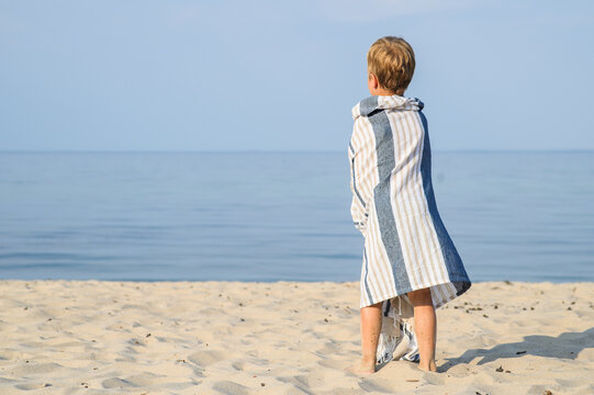 Young Boy Wrapped in Striped Beach Towel Looking at Calm Water