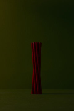 Minimalist studio shot of a spiral tower formed by dark red wooden pencils, set against a dark olive green background with ample negative copy space and subtle, dramatic lighting.