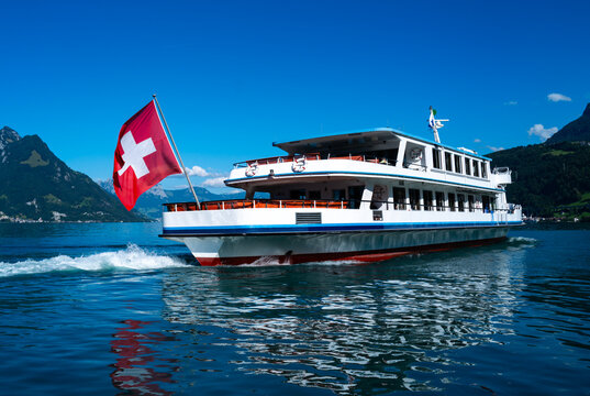 Swiss tourism offers Lake Lucerne boat cruises. Swiss tourism presents white ship in Switzerland. Tourism offers Swiss boat travel across Lucerne. Tourism displays Swiss flag on passenger ship.