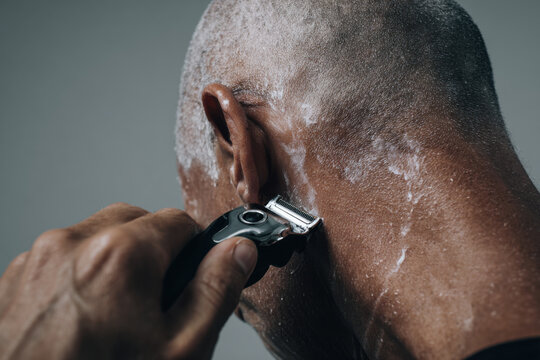 Close-up of a man shaving his head with an electric razor and foam