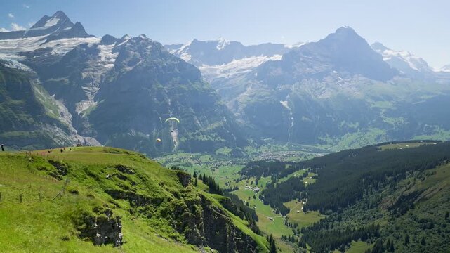 Scenic view of paragliders soaring over a green valley in the grindelwald area of switzerland. Switzerland