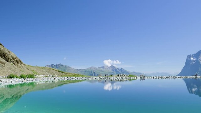 Beautiful mountain landscape reflecting in the calm, clear water of an alpine lake on a sunny day. Switzerland