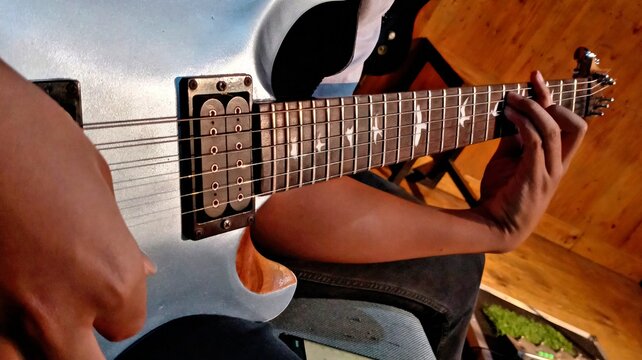 Musician Hands Playing Electric Guitar in Music Studio Close Up
Close-up shot of a guitarist's hands playing chords on a silver metallic electric guitar with bird fretboard inlays. Warm studio.