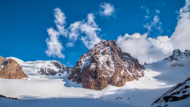 Rocky alpine ridge with lingering snow patches illuminated by soft morning light as clouds drift over Bogdanovich Glacier in the Ile Alatau mountains of Kazakhstan.