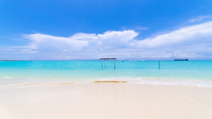 Fototapeta premium Wooden swing standing in the shallow turquoise lagoon on Maamigili Island with gentle waves and dramatic clouds over the Indian Ocean.