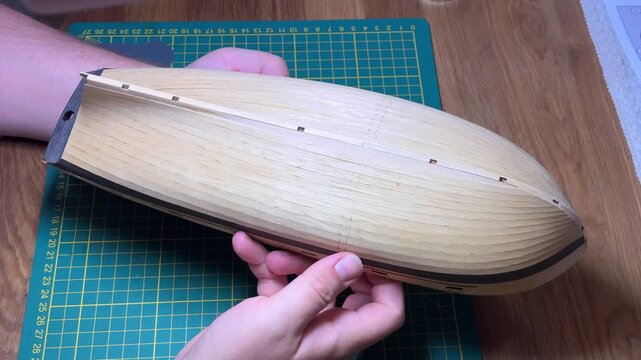 Hands holding assembled wooden boat hull scale model, showcasing detailed craftwork, DIY boat modeling.