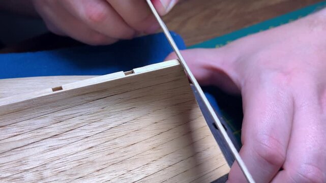 Hands sanding wooden deck planking on scale model boat, meticulous craftsmanship, DIY boat modeling.