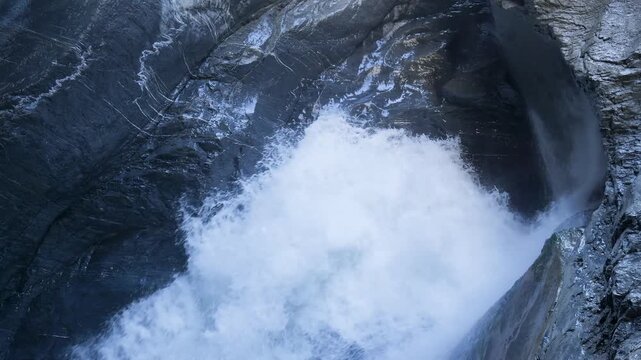 White water rapids from a powerful waterfall flowing through a narrow and dark stone gorge. Switzerland