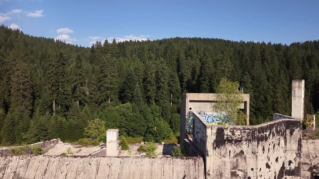 Aerial Top Down View of Abandoned War Ruined Hotel Igman with Trees Growing Inside Structure Surrounding Pine Forest Bosnia
