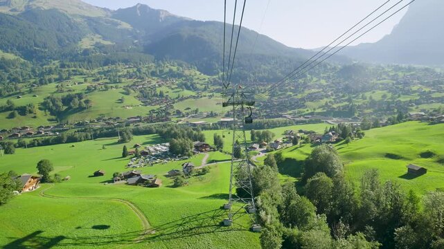 Gondola ascending over the green swiss alpine valley of grindelwald on a sunny summer day. Switzerland