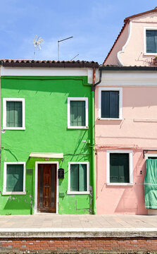 Vibrant green and pink adjoining house facades with wooden shutters and doors in Burano, Venice, Italy