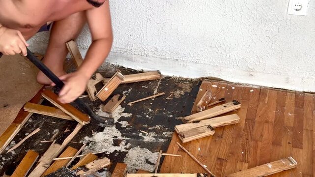 Hands Removing Old Wooden Flooring with Crowbar During Home Renovation