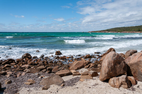Ocean waves breaking around large granite boulders along a remote rocky shore on a sunny day