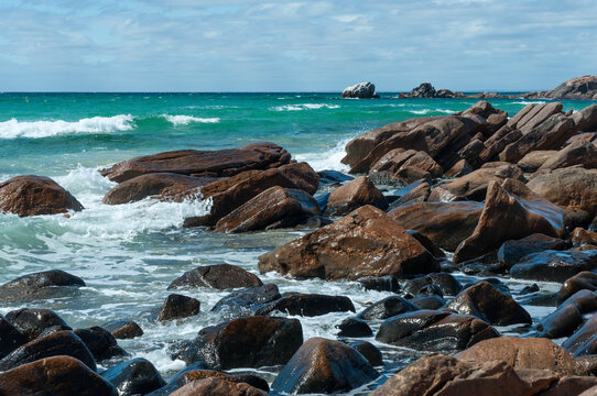 Turquoise ocean waves breaking over wet granite boulders along a rugged rocky coastline