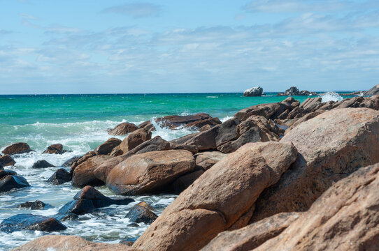 Scenic seascape with clear aquamarine water, weathered rocks, white surf and spacious cloud-filled sky