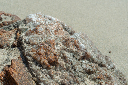 White quartz crystals embedded in weathered coastal rock, showing rusty brown mineral staining and a rough natural texture