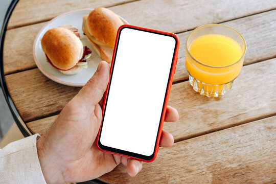Mockup man's hand holding using smart phone with white blank screen POV at coffee shop, mobile app design and advertising, online marketing	