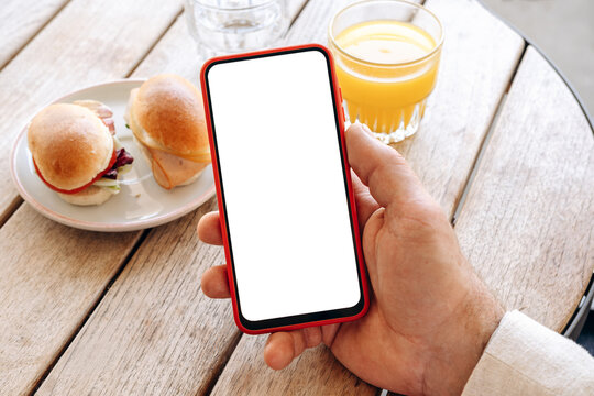 Mockup man's hand holding using smart phone with white blank screen POV at coffee shop, mobile app design and advertising, online marketing	