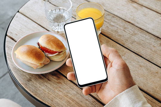 Mockup man's hand holding using smart phone with white blank screen POV at coffee shop, mobile app design and advertising, online marketing	