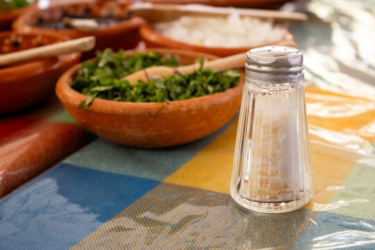 Glass salt shaker on traditional Mexican restaurant table with condiments background