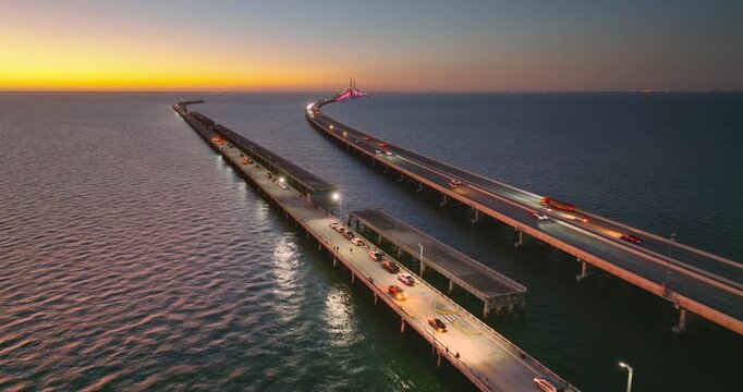 Transportation infrastructure of Florida, USA. Sunset above Sunshine Skyway Bridge over Tampa Bay with driving traffic cars and fishing pier