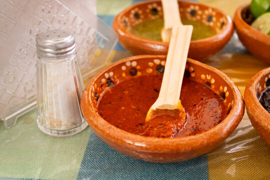 Red Mexican salsa in traditional clay bowl with wooden spoon on table