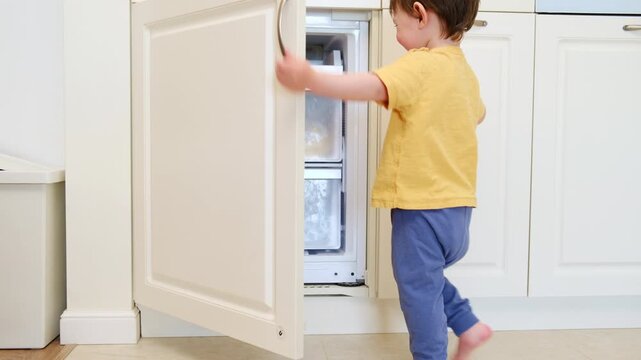 Child opening freezer drawer in kitchen. Toddler curious about household appliance. Domestic life with kid exploring home. Safety concept and childhood growth in contemporary house.