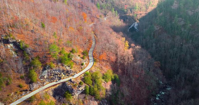 Vibrant woods surround a car driving near Cullasaja Falls. Highlands Road provides a scenic journey through North Carolina