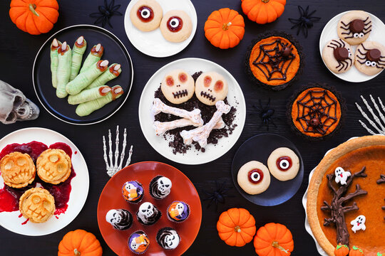 Fun Halloween dessert table scene over a black wood background. Top view. Selection of cookies, cupcakes and pumpkin and apple tarts and pies.