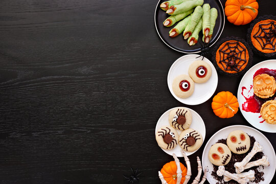 Fun Halloween dessert side border over a black wood background with copy space. Top down view. Variety of cookies, cupcakes and pumpkin and apple tarts and pies.