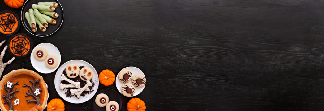 Fun Halloween dessert corner border over a black wood banner background with copy space. Top view.  Assortment of cookies, cupcakes and pumpkin and apple tarts and pies.