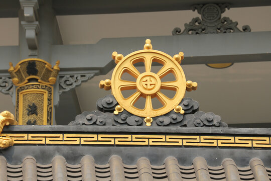 Golden Dharmachakra Wheel of Dharma symbol on a traditional Buddhist temple roof.