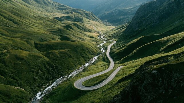 Winding road curves gracefully through a lush green alpine valley flanked by steep grassy mountains under soft daylight in a remote countryside landscape.