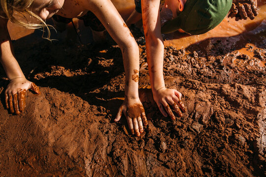 Children's hands playing in red mud