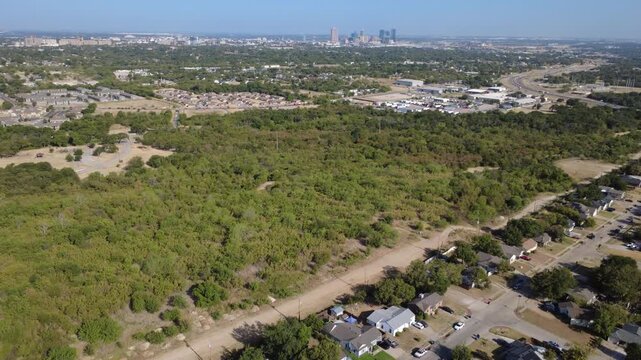 Vast natural forest expanses meet quiet residential streets across Tarrant County. Single-story suburban rooftops blend into dense green woodland belts under sun, Fort Worth, Texas