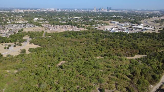 Sprawling nature preserves blanket Cobb Park greenways across DFW Metroplex. Rich forest canopies frame distant downtown skyscraper silhouettes under sunny skies, Fort Worth, Texas